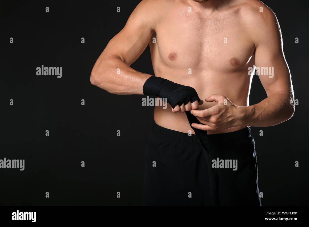 Strong male boxer applying wrist bands against dark background Stock
