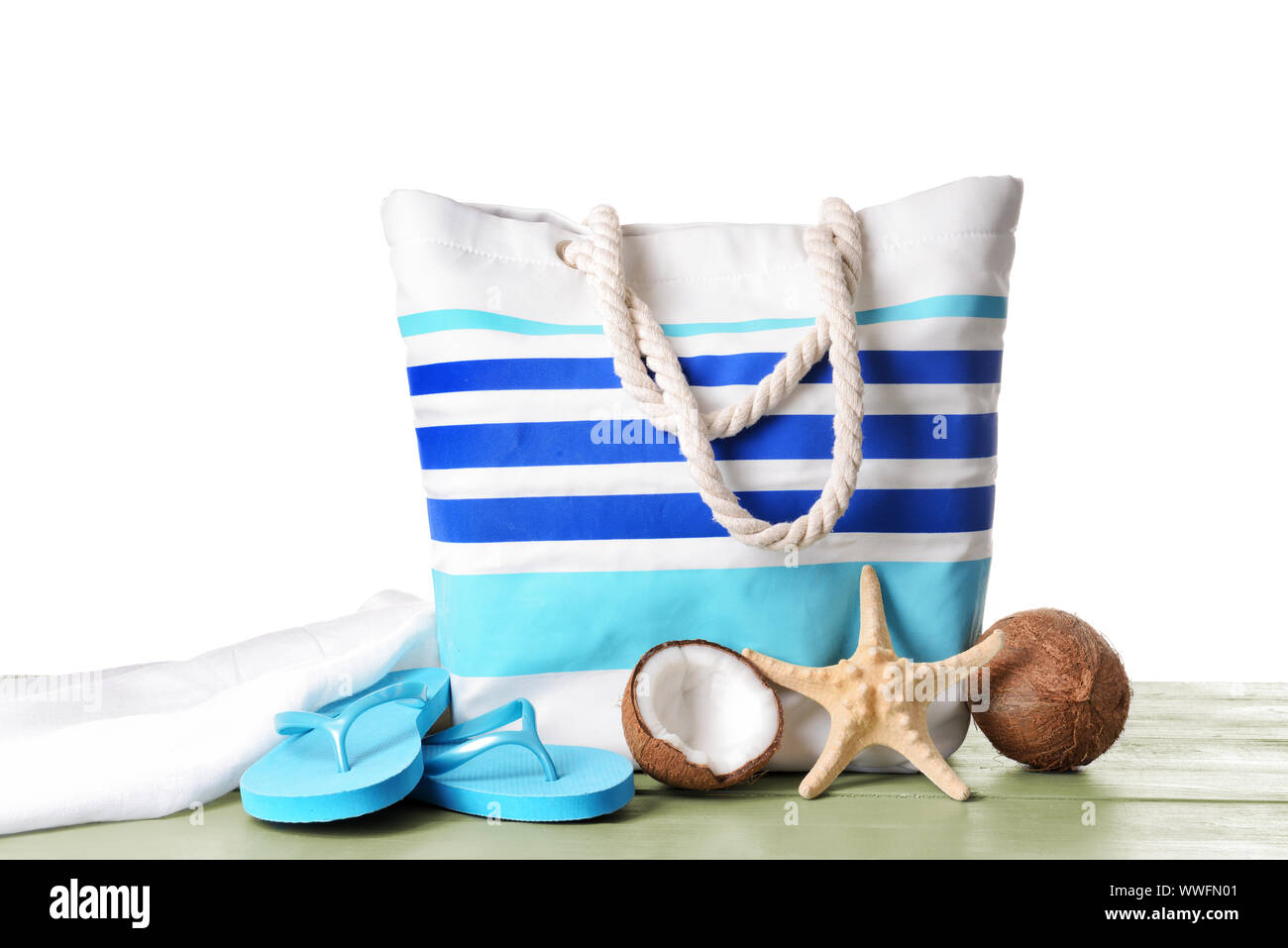 Beach bag, coconuts, flipflops and starfish on table against white