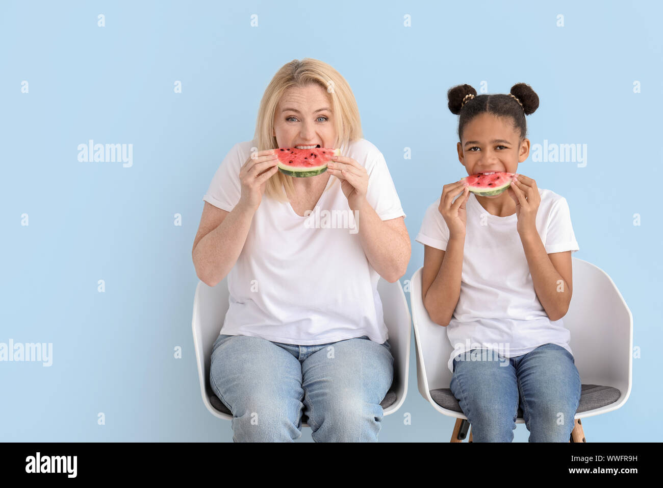 Happy woman with her African-American daughter eating watermelon on ...