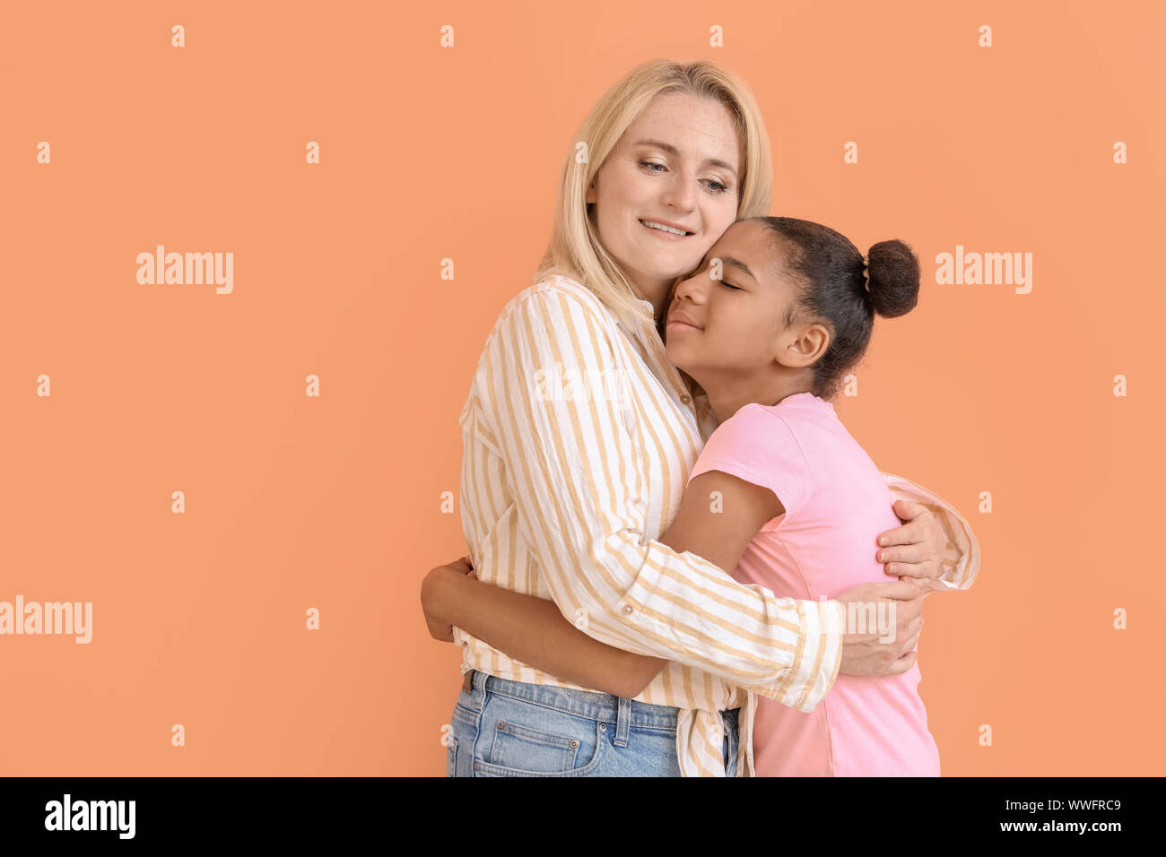 Happy woman hugging her African-American daughter on color background ...