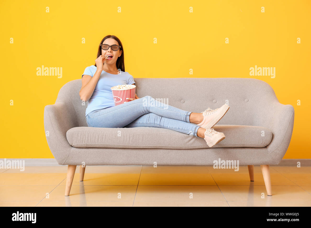 Young woman with popcorn watching movie on sofa near color wall Stock ...