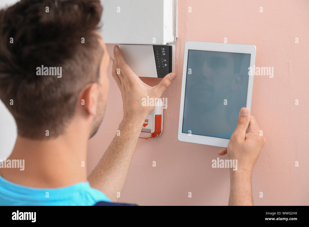 Electrician with tablet computer checking alarm system indoors Stock Photo