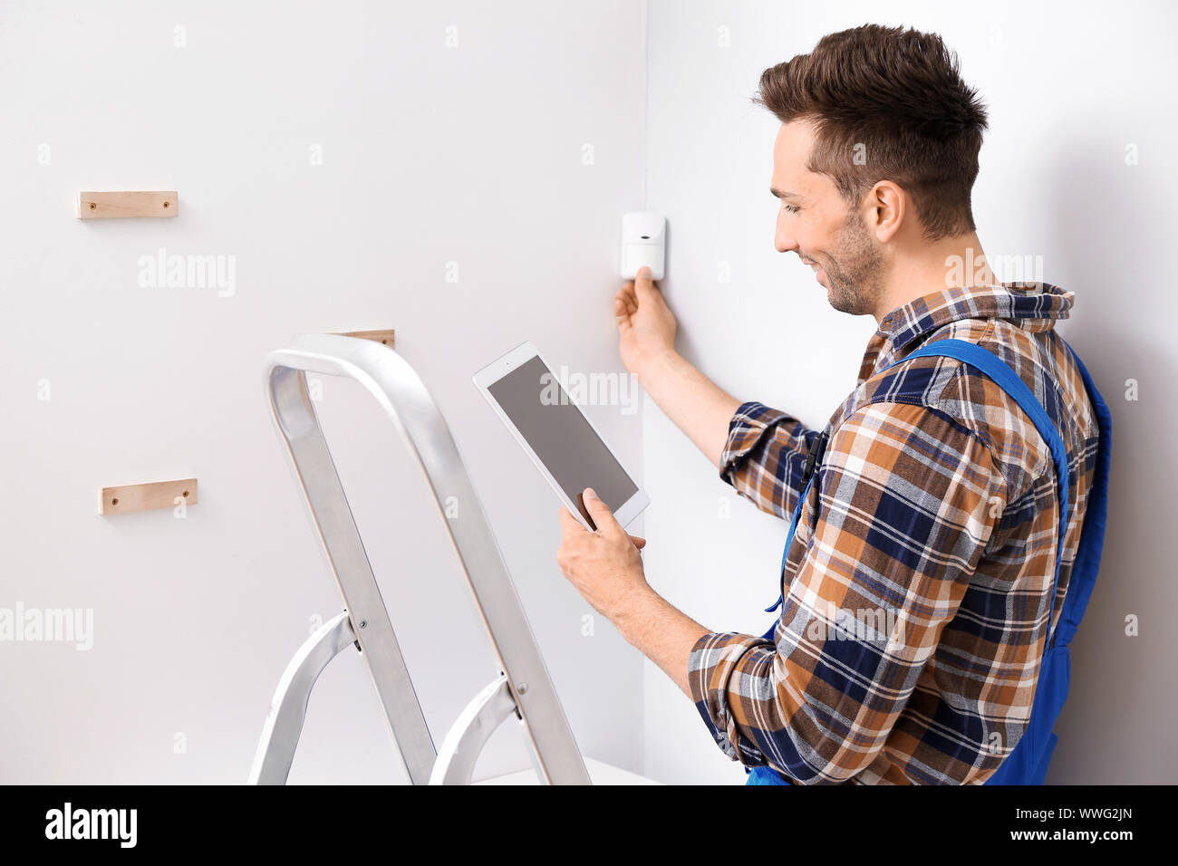Electrician with tablet computer installing alarm system indoors Stock Photo