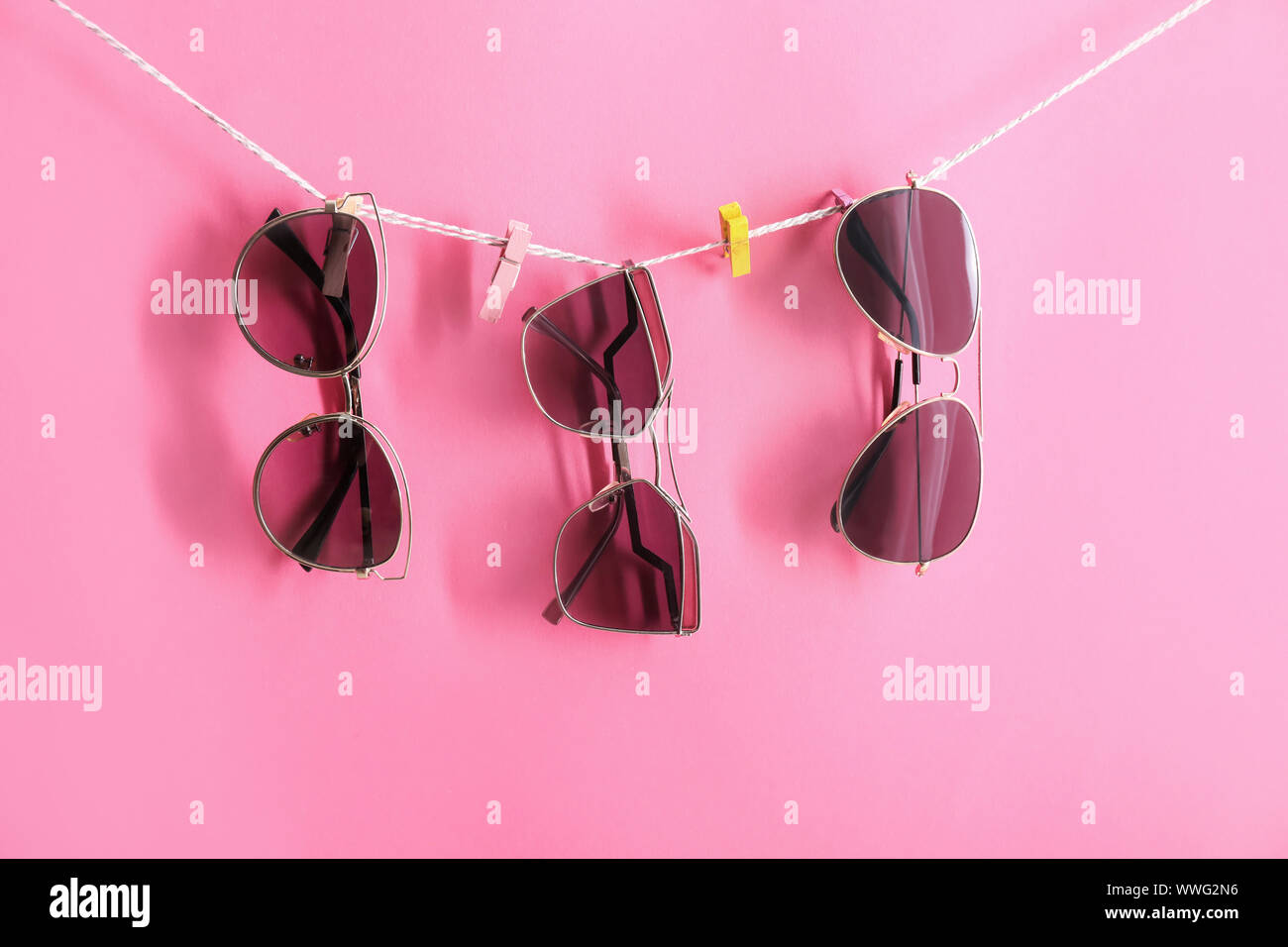 Stylish sunglasses hanging on rope against color background Stock Photo