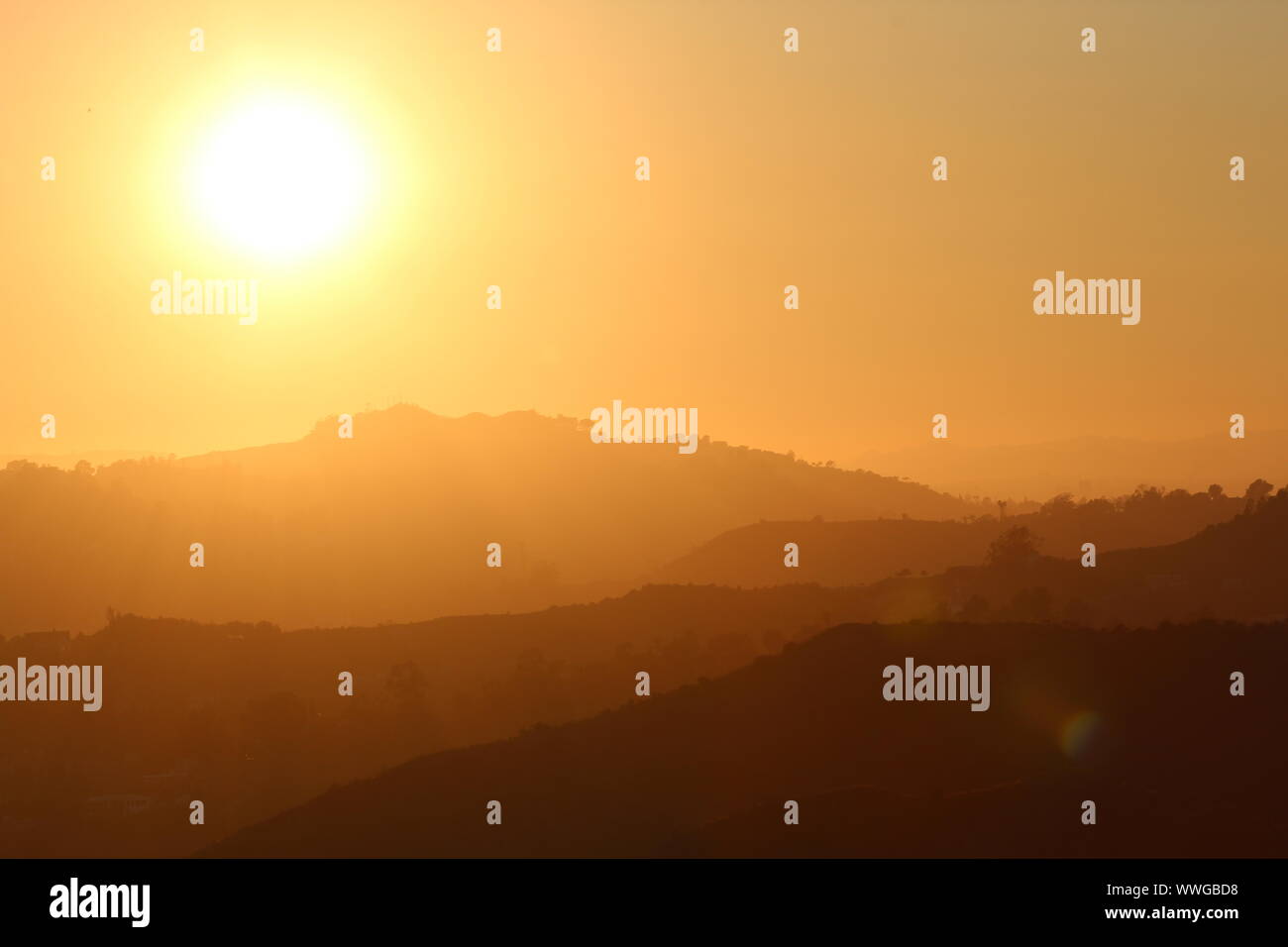 bright yellow sun by a silhouette of layers of mountains as seen in Hollywood CA Stock Photo