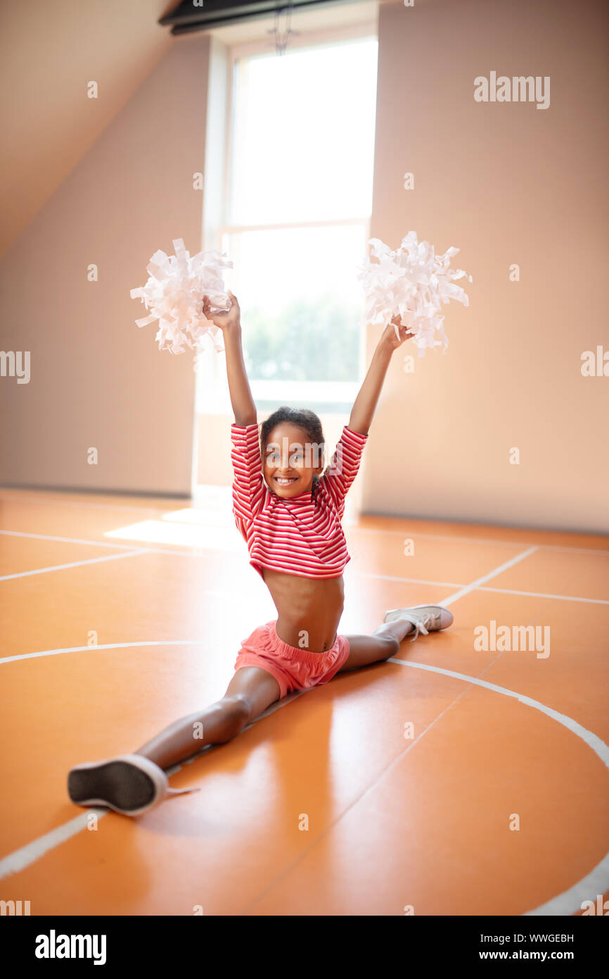 Positive dark-skinned cheerleader doing leg split Stock Photo