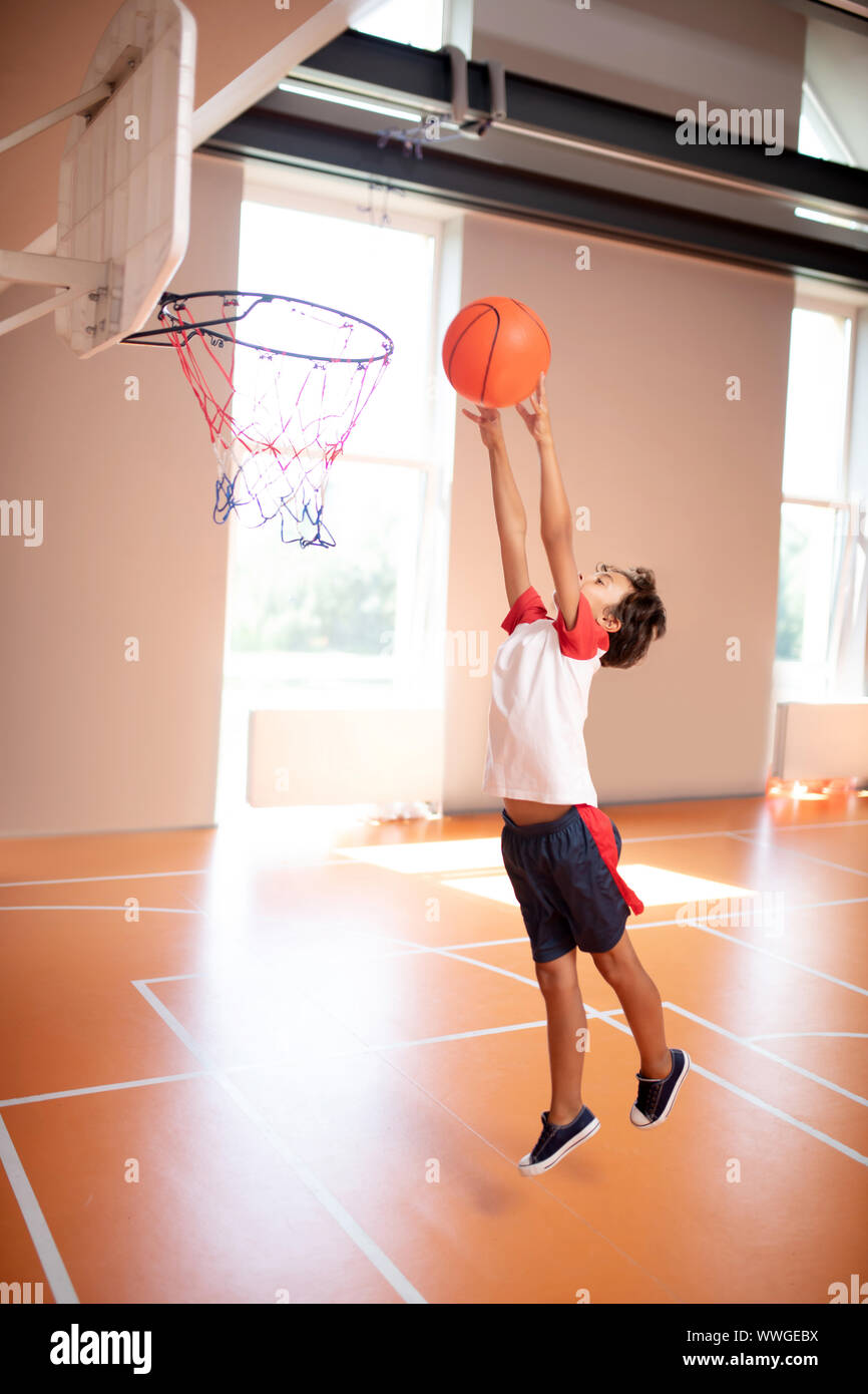 Schoolboy wearing sport clothing throwing ball into basket Stock Photo