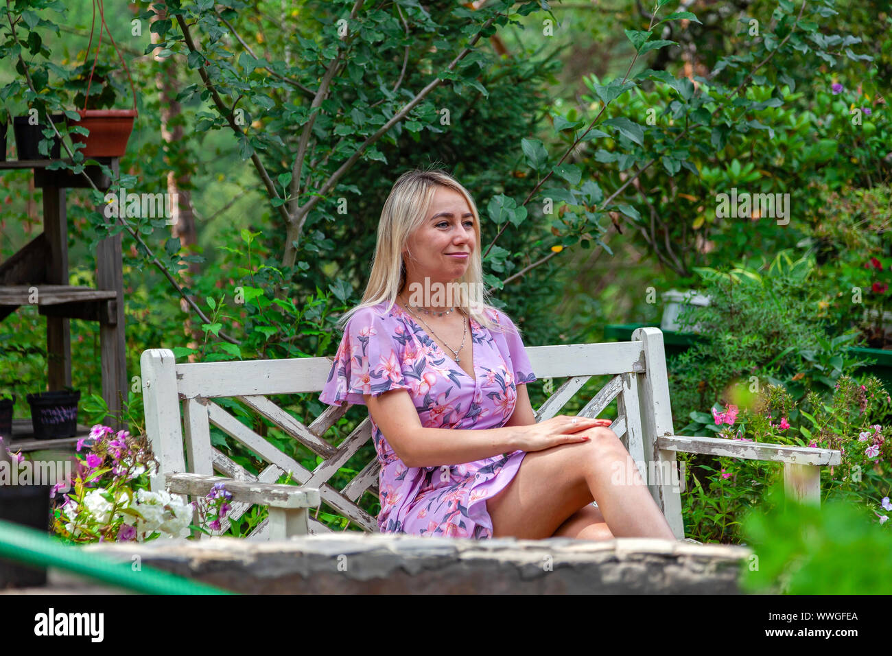 A young blonde girl in a pink dress sits on a white wooden bench in the ...