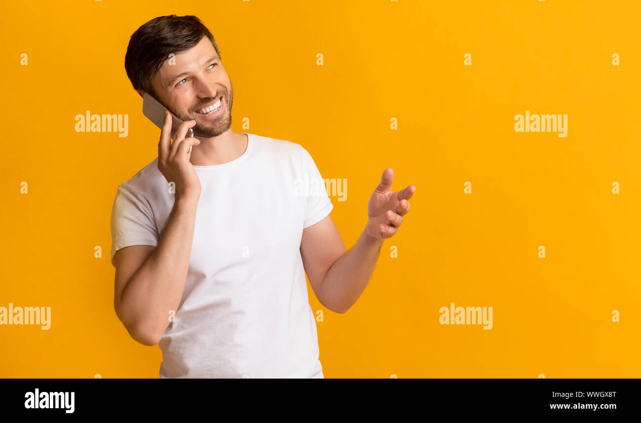 Happy Man Talking On Phone Standing On Yellow Background Stock Photo