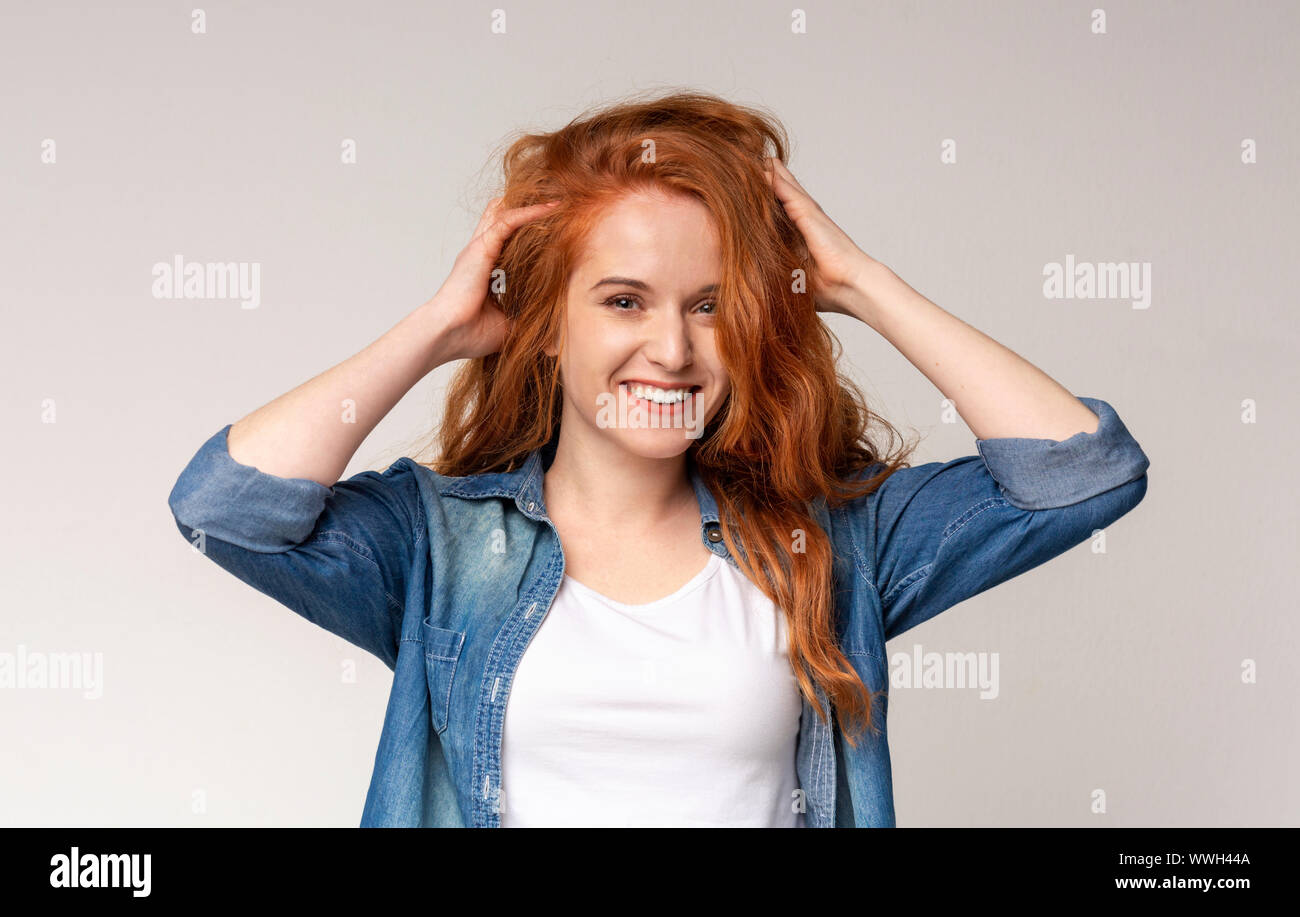 Happy redhead girl smiling and touching her beautiful curly hair Stock Photo