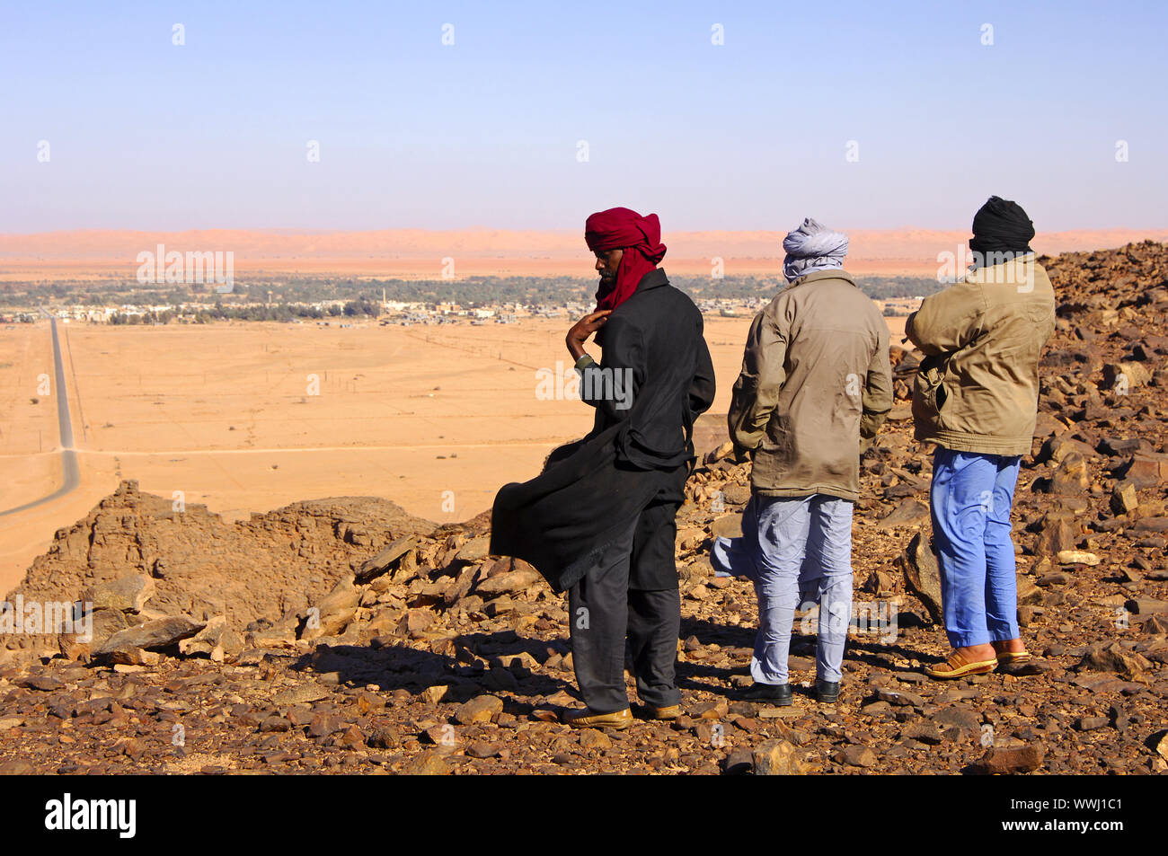 Native men in Arabic dress with traditional headscarf looking from a hill to the desert town of Germa in the plain Stock Photo