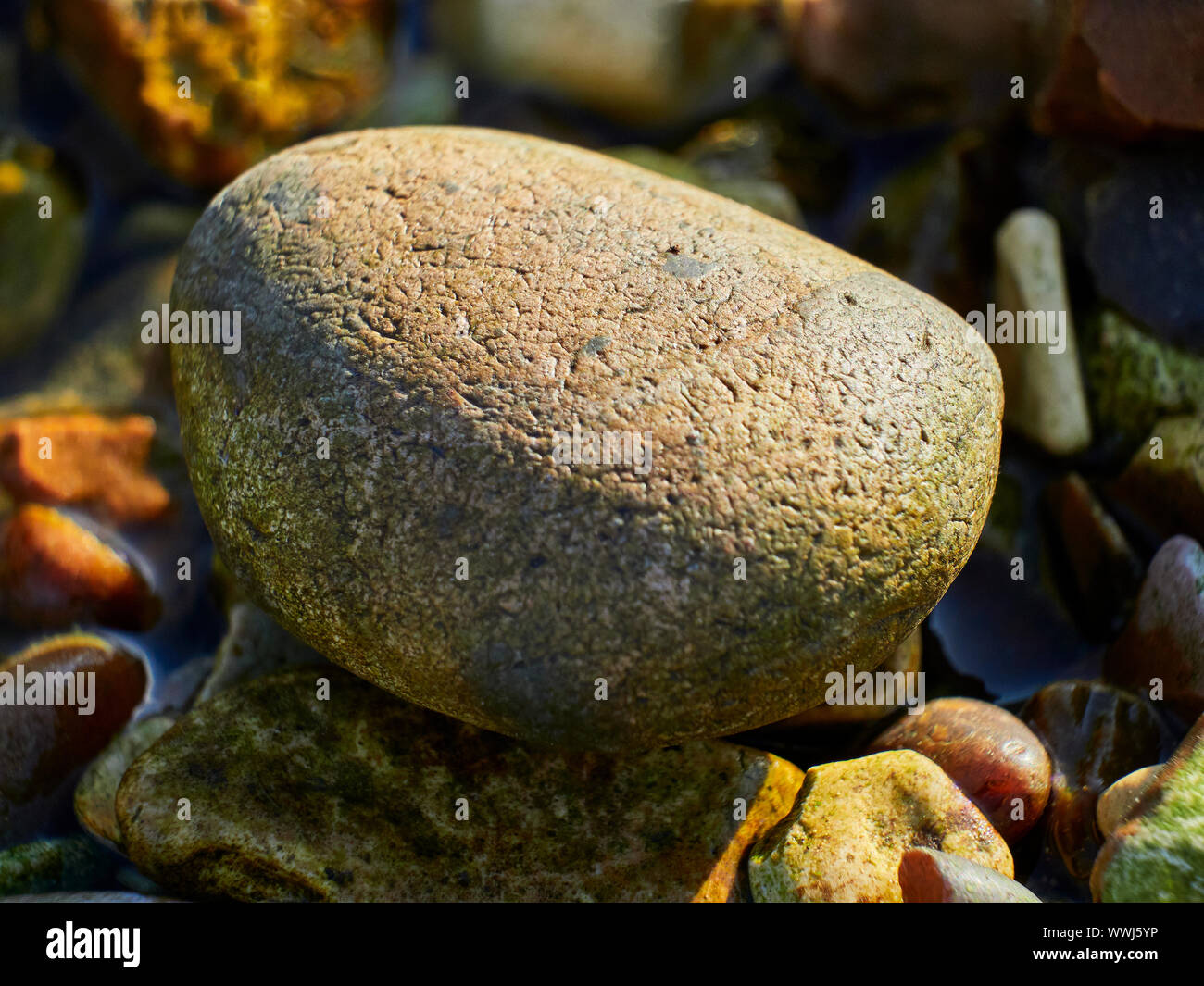 A large smooth pebble sat on top of a number of smaller different colour and shaped pebbles Stock Photo
