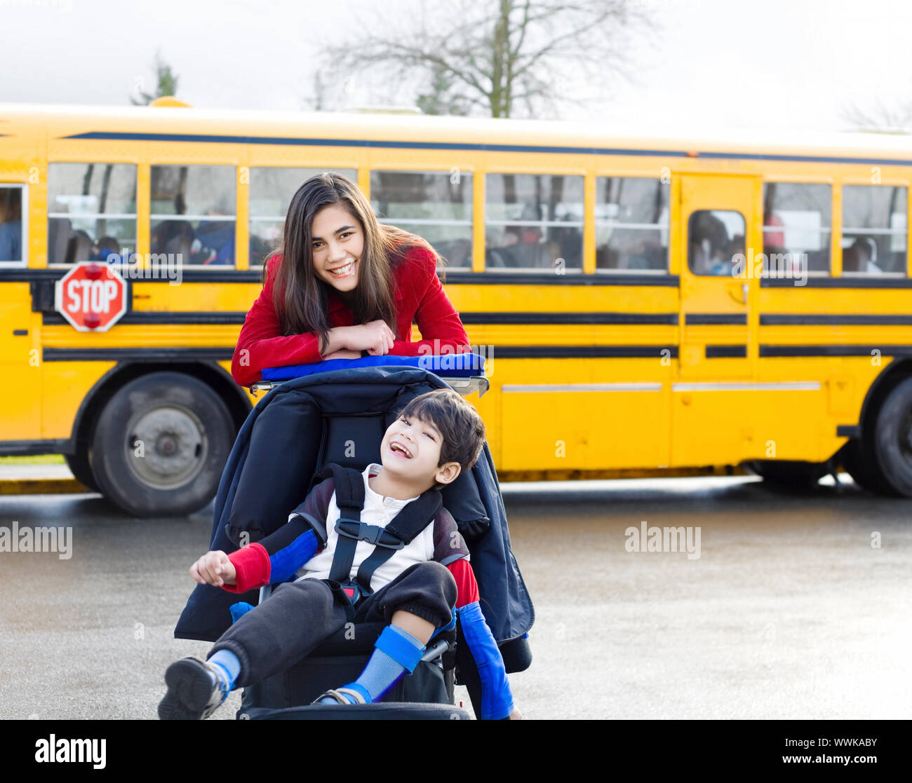 Big sister with disabled brother in wheelchair by school bus Stock Photo