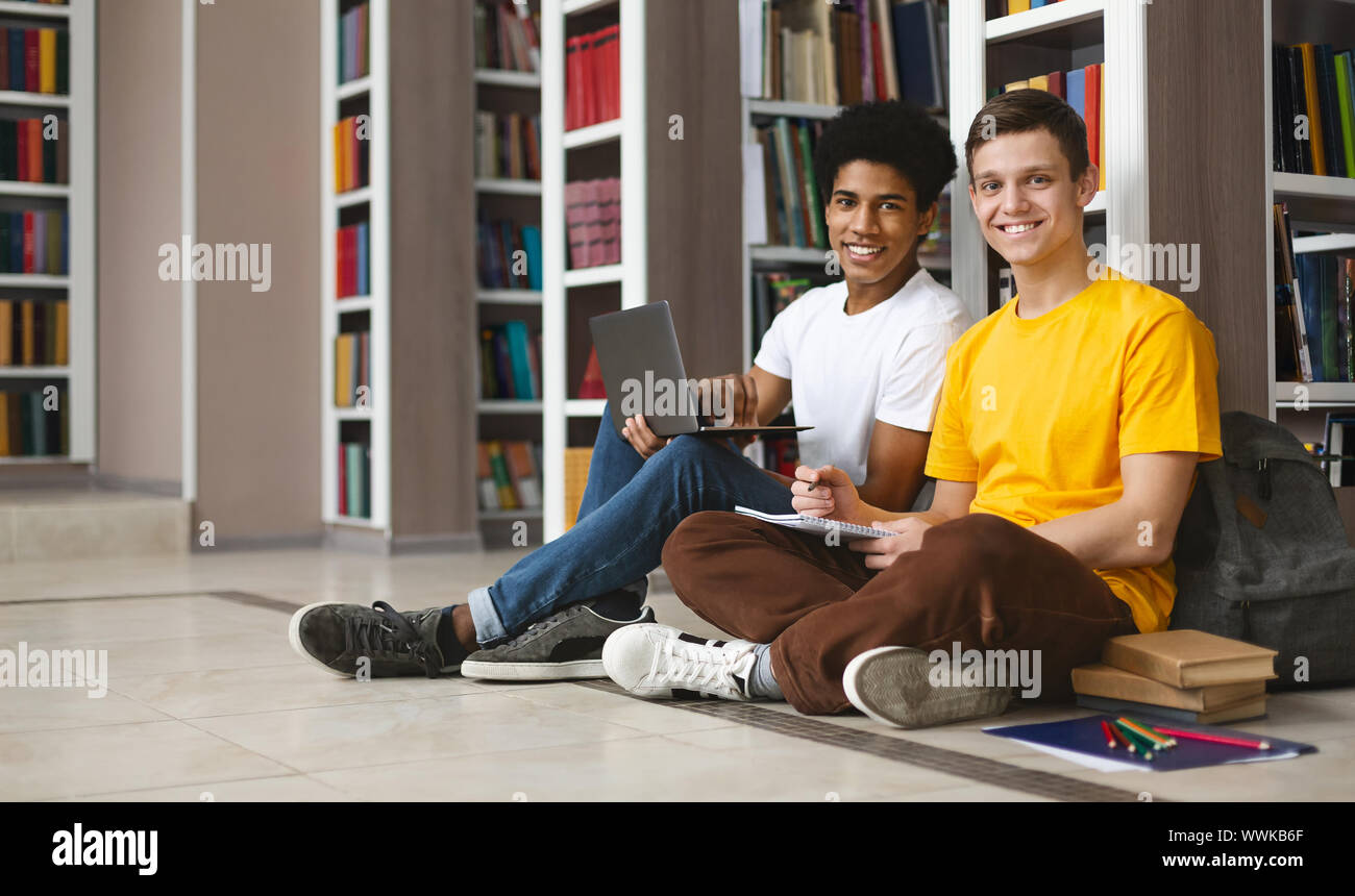 Two guys studying on floor in library, smiling at camera Stock Photo