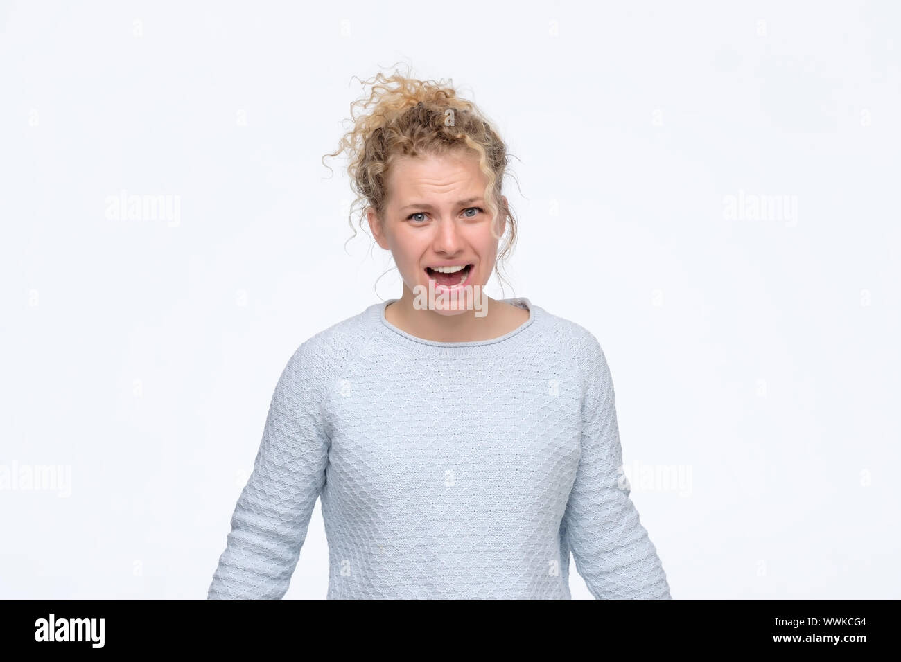Angry blonde curly woman screaming in quarrel with her boyfriend. Studio shot. Stock Photo