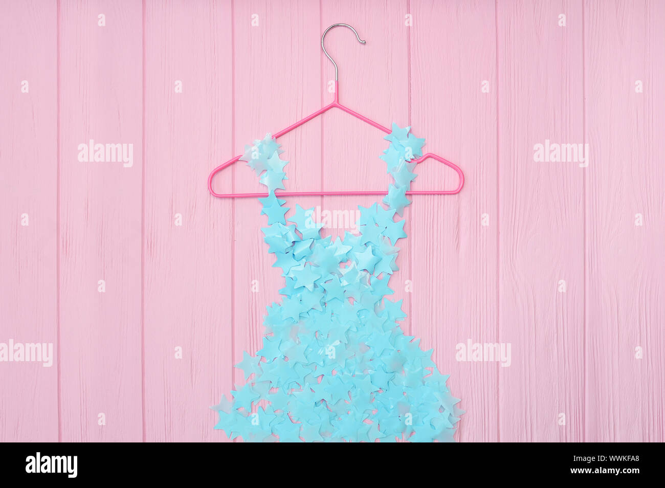 Blue girls stylized dress from stars confetti hanging on red trempel on pink wooden background. Fashion concept Stock Photo