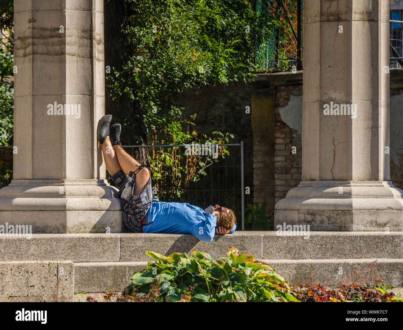 Man lying on back in sun making phone call. Stock Photo