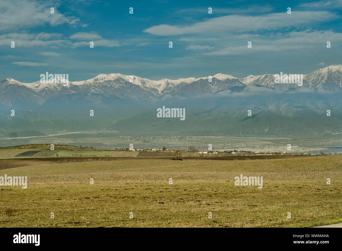 Mountain village with snowy peaks in the background and gold color meadow in foreground. Stock Photo