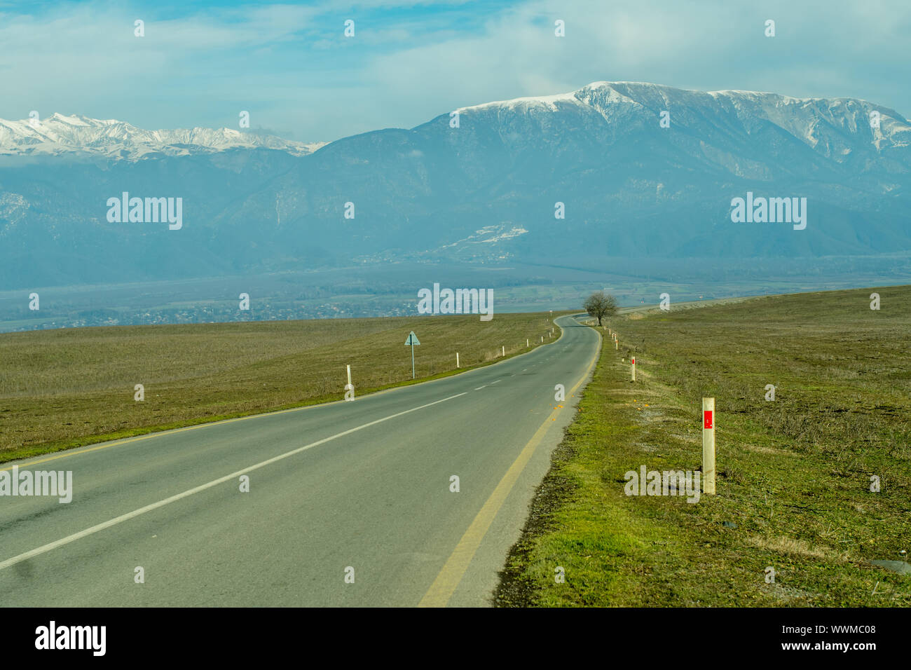 Mountain village with snowy peaks in the background long asphalt road in foreground. Stock Photo