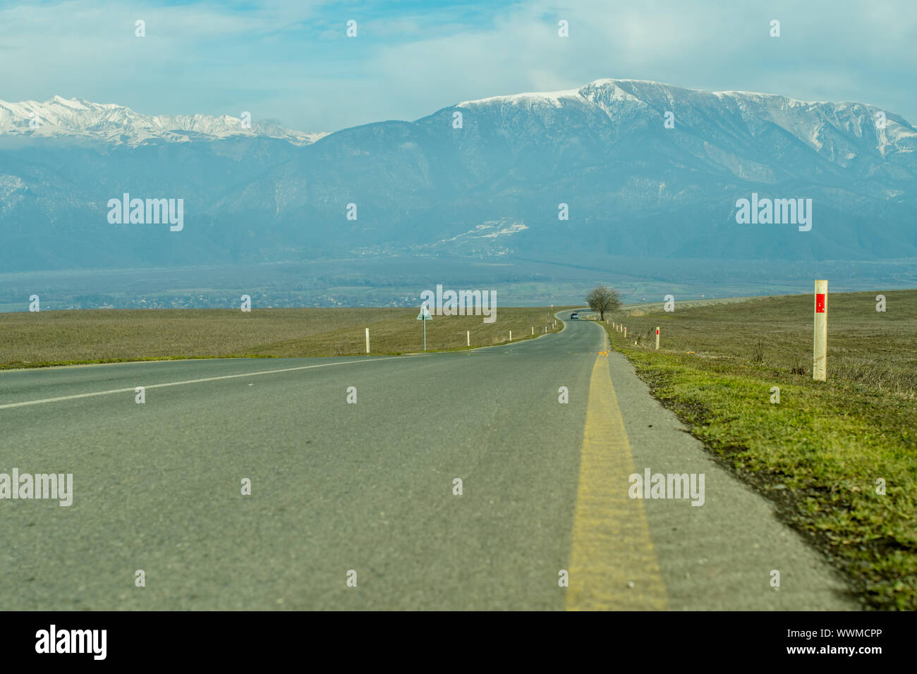 Mountain village with snowy peaks in the background long asphalt road in foreground. Stock Photo