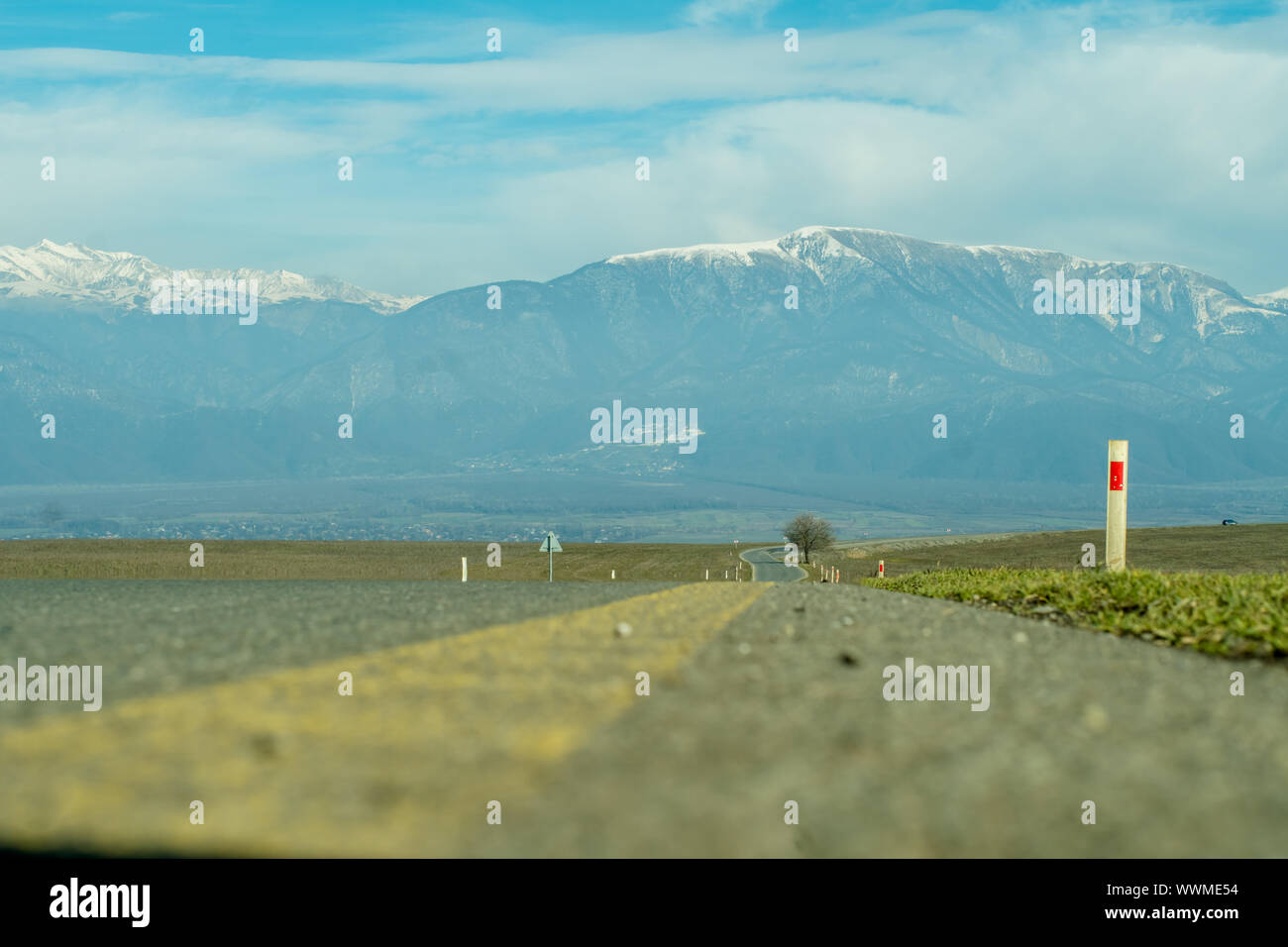 Mountain village with snowy peaks in the background long asphalt road in foreground. Stock Photo