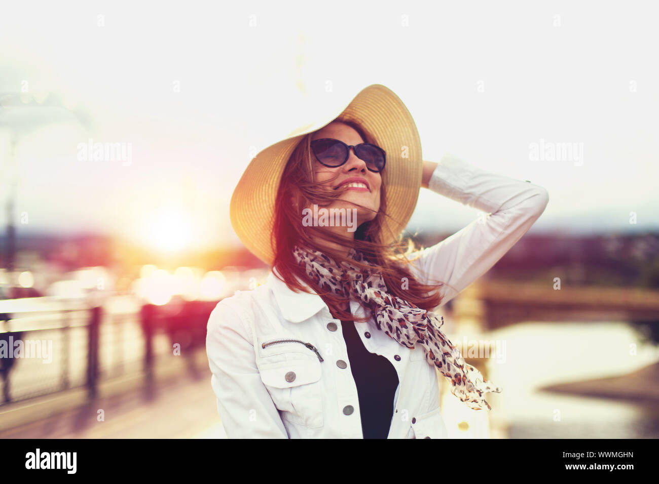 Happy young trendy woman in hat looking up in sunset Stock Photo