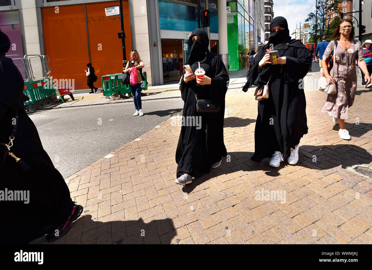 London, England, UK. Muslim women wearing the Niqab and training shoes in Oxford Street, with mobile phones and takeaway drinks Stock Photo