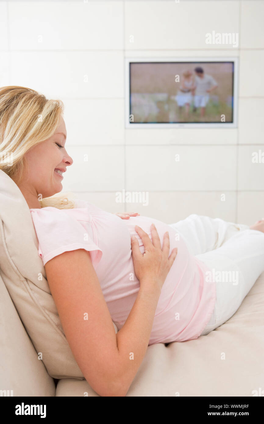 Pregnant woman watching television smiling Stock Photo - Alamy