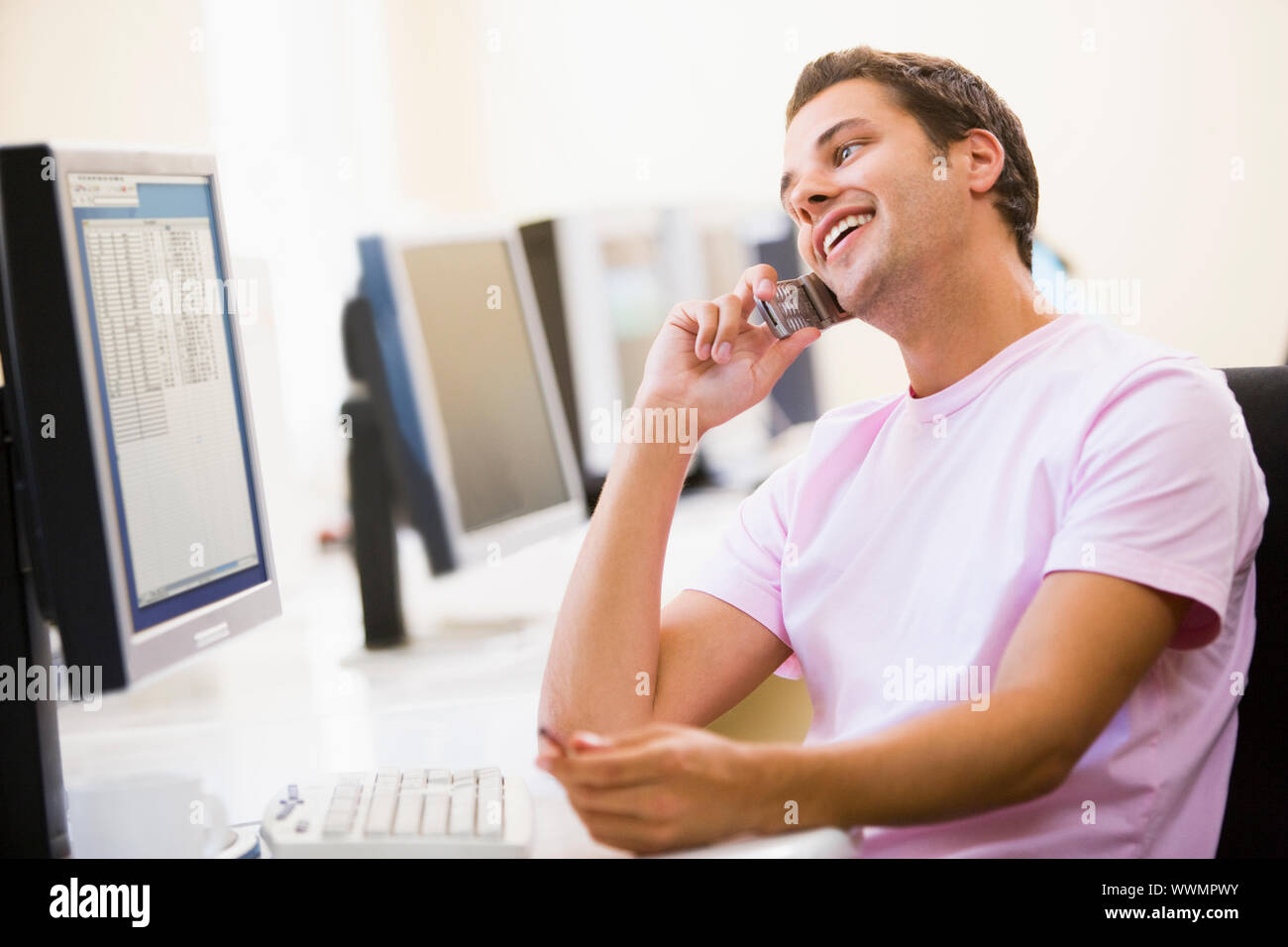 Man sitting in computer room using cellular phone and smiling Stock Photo