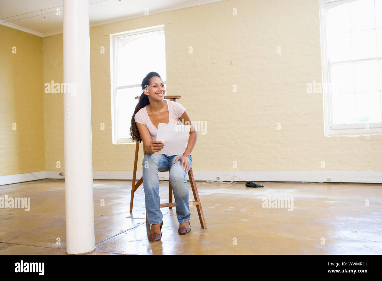 Woman sitting on ladder in empty space holding paper Stock Photo