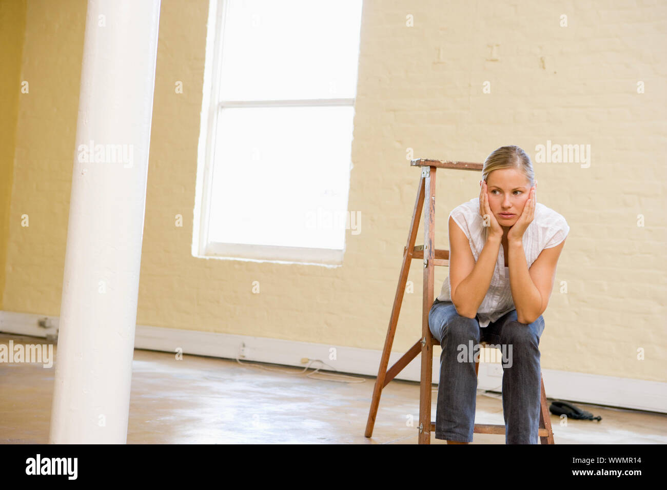 Woman sitting on ladder in empty space looking bored Stock Photo