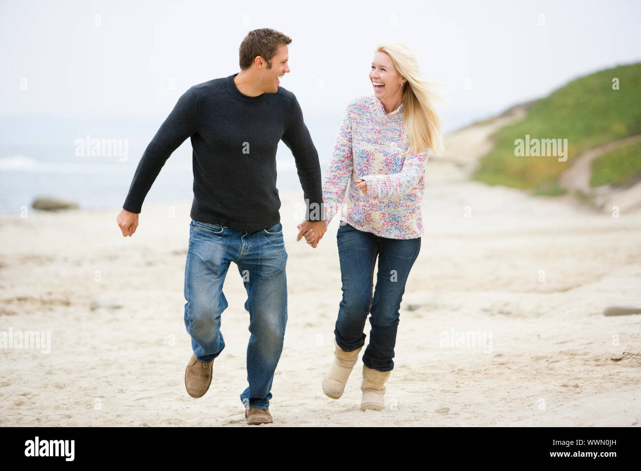 Couple running at beach holding hands smiling Stock Photo - Alamy