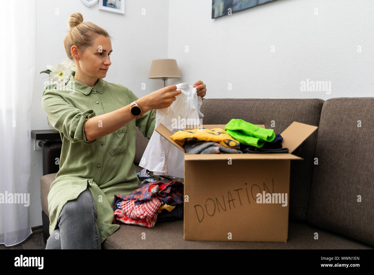 mother sitting on couch and sorting child clothes for donation Stock Photo