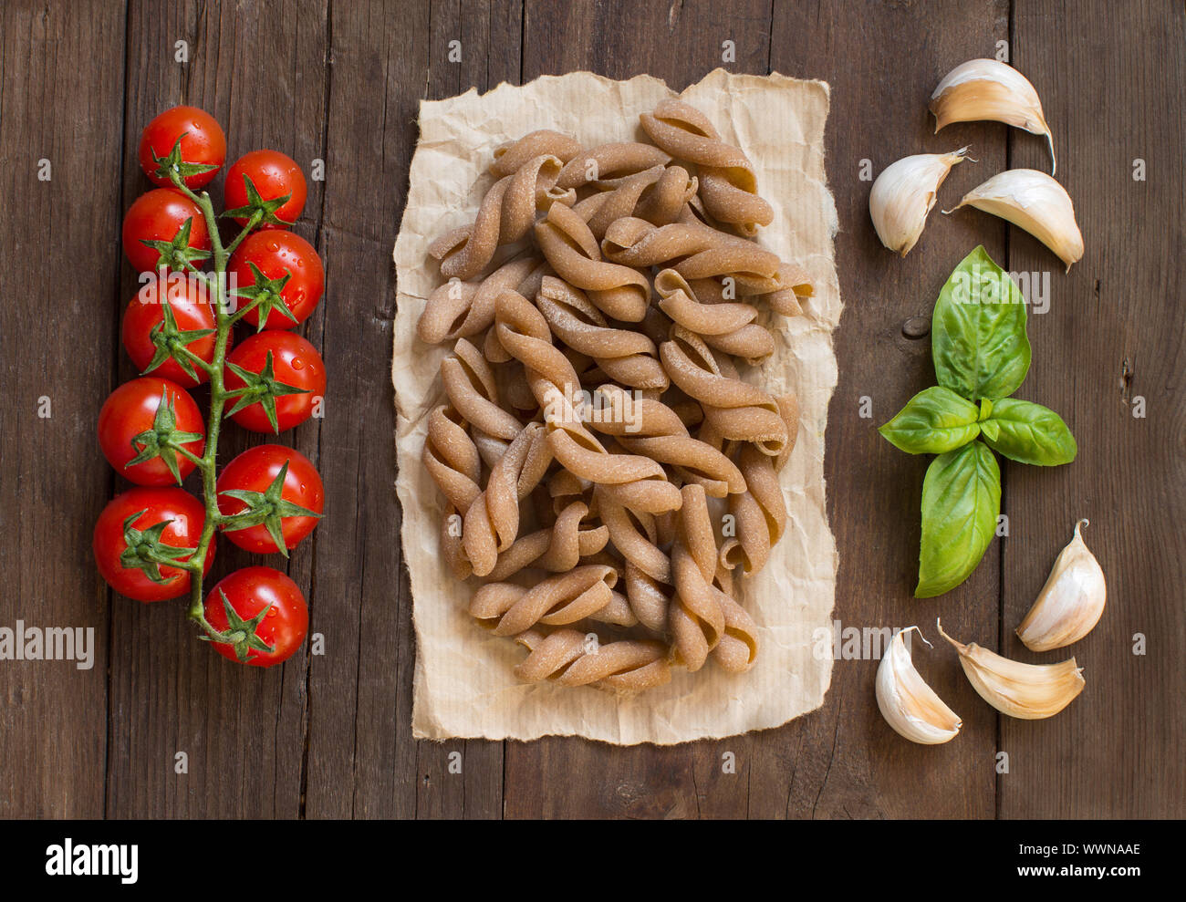 Whole wheat pasta, tomatoes and basil on wooden background Stock Photo