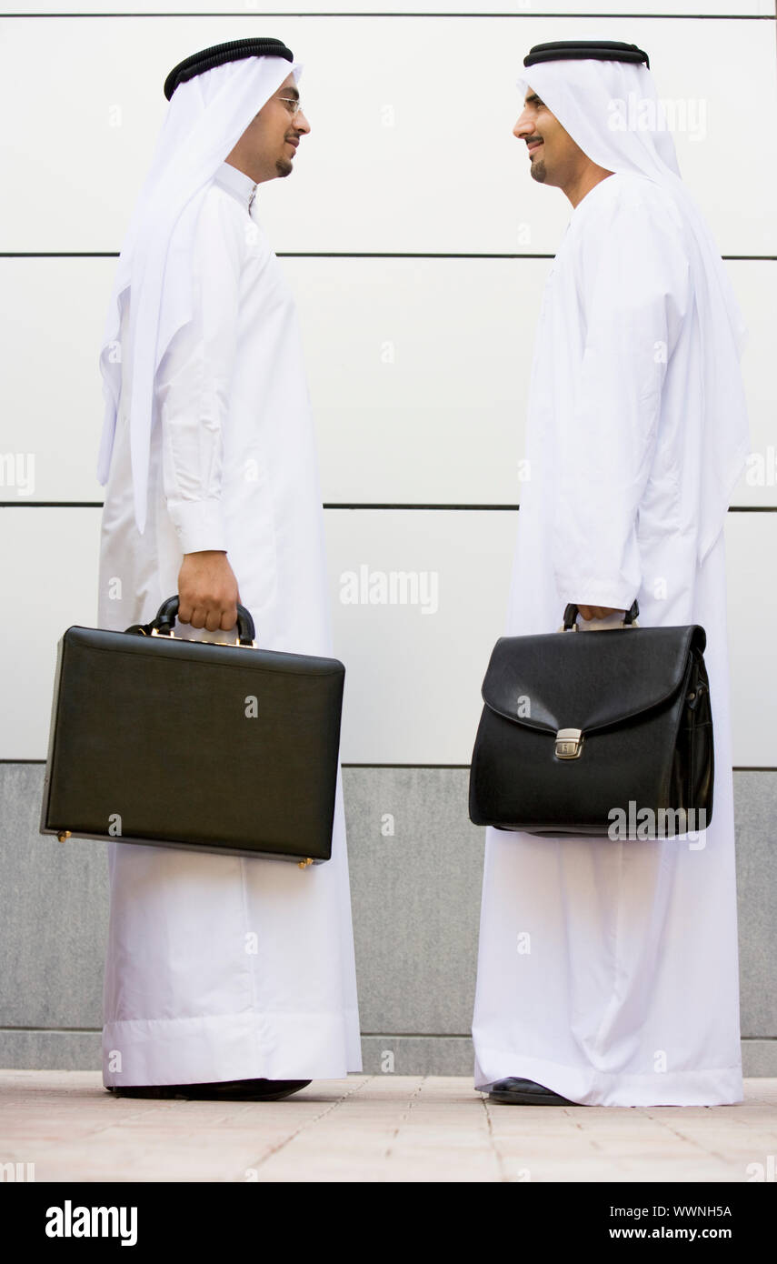 Two businesspeople standing outdoors with briefcases smiling Stock Photo