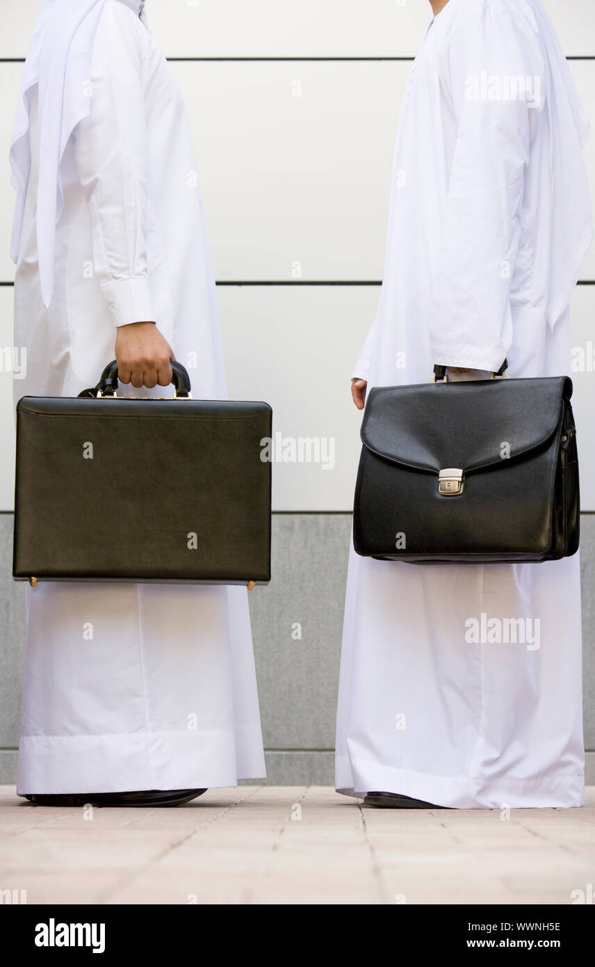 Two businesspeople standing outdoors with briefcases smiling Stock Photo