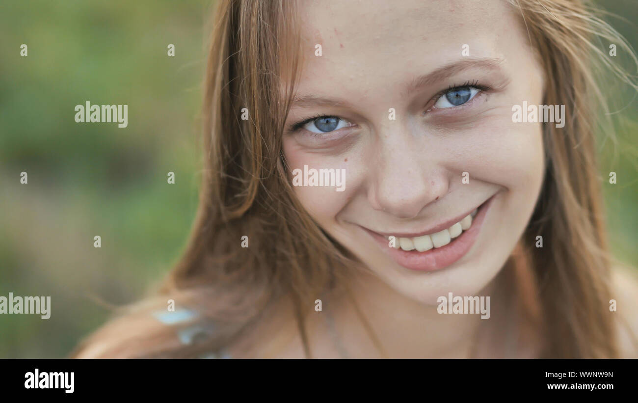 Portrait of a young smiling sixteen-year-old girl with a daisy flower in her hands. Brown-haired girl with long hair.. Face close-up. Stock Photo