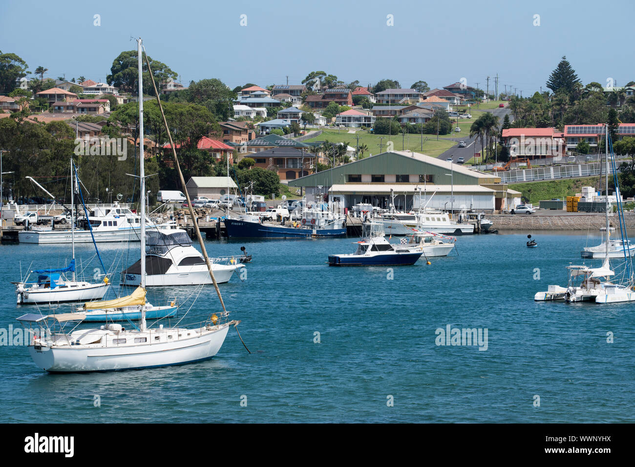 Large fishing trawlers and smaller recreational boats are moored in the harbour and at the marina in front of the Ulladulla Fisherman Co-op building. Stock Photo