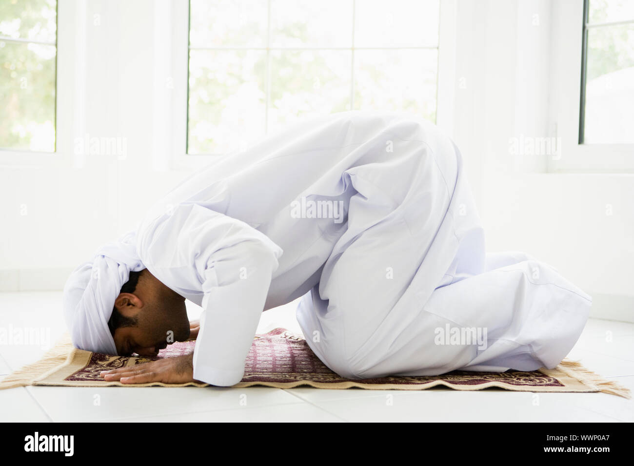 Man indoors praying on mat (high key) Stock Photo