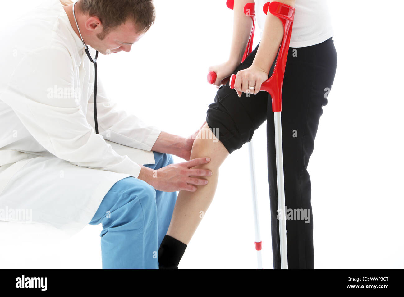 Orthopaedic surgeon sitting examining the knee of a female patient on crutches following surgery
