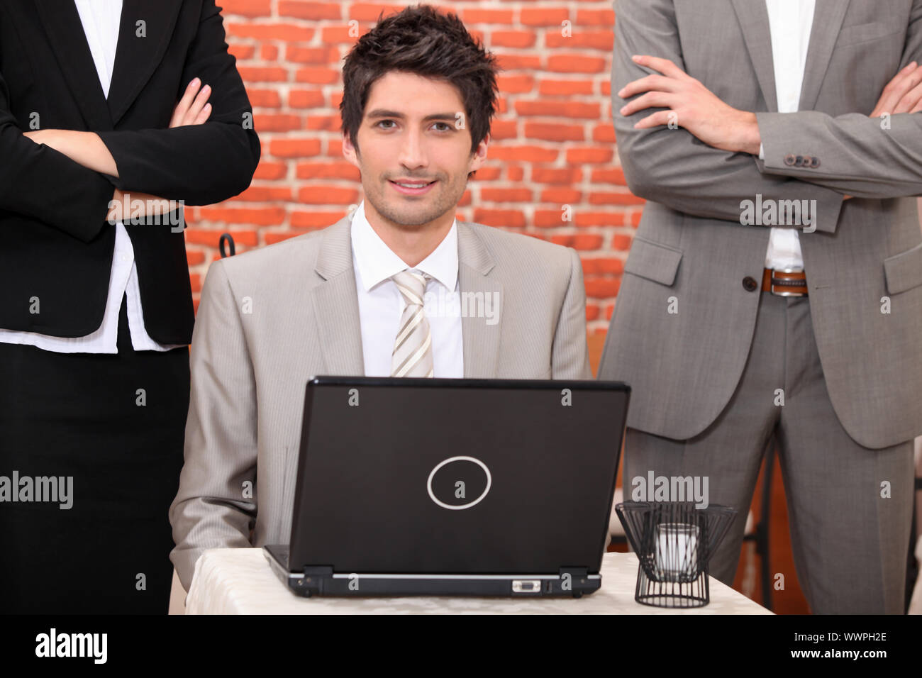 Man using a laptop flanked by people in suits Stock Photo