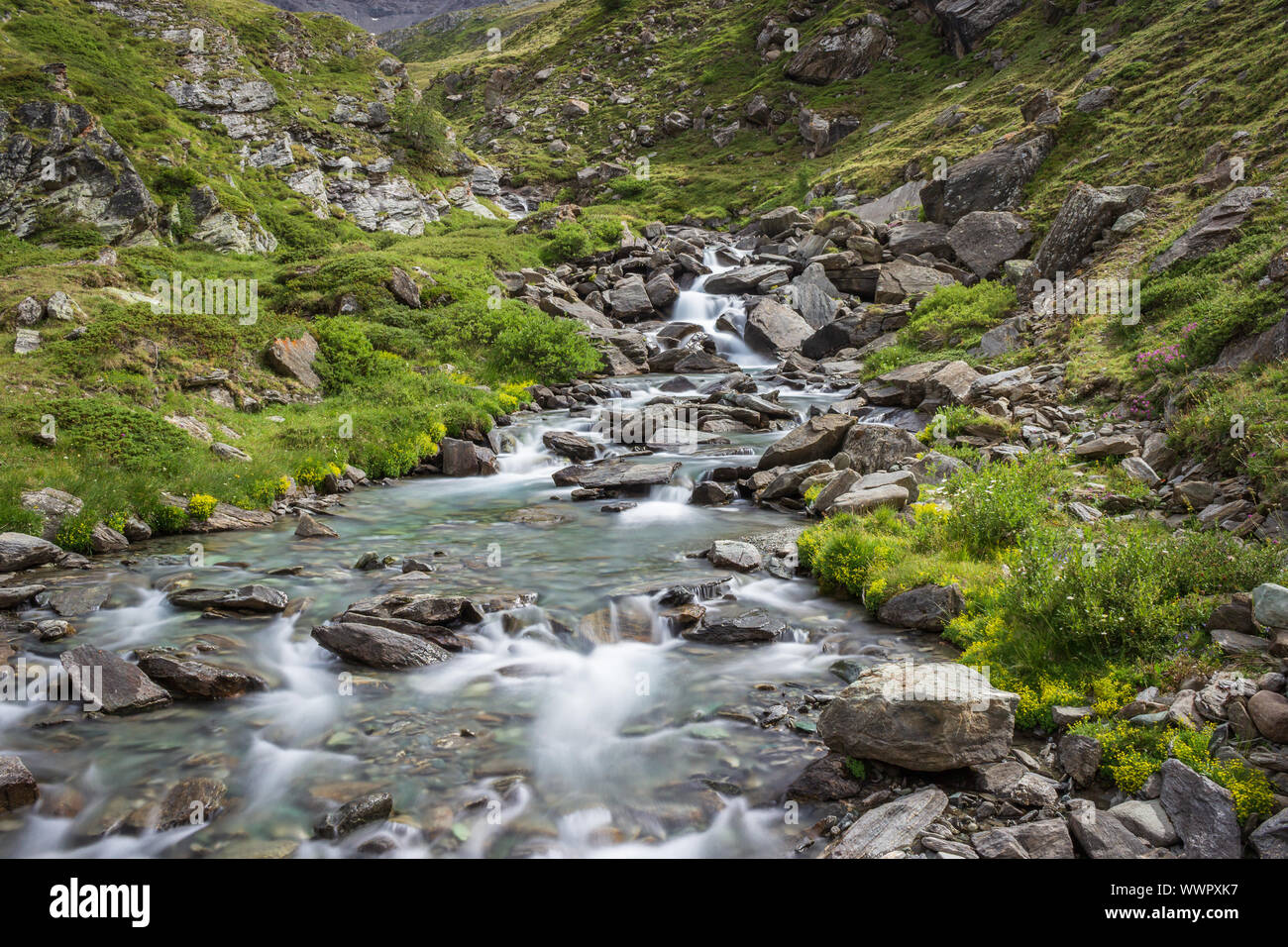 Hiking trail in Aosta valley with wild mountain stream landscape. Long exposure shot. Stock Photo