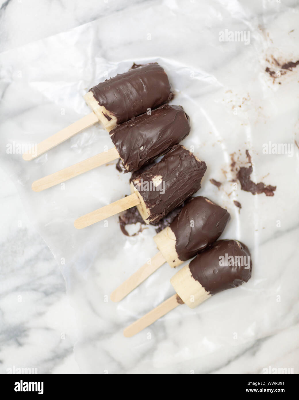 Bananas covered in chocolate and peanut butter lying on marble counter