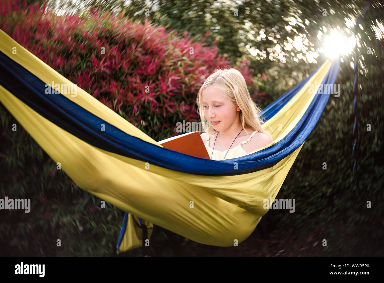 Adolescent girl reading in a yellow hammock Stock Photo