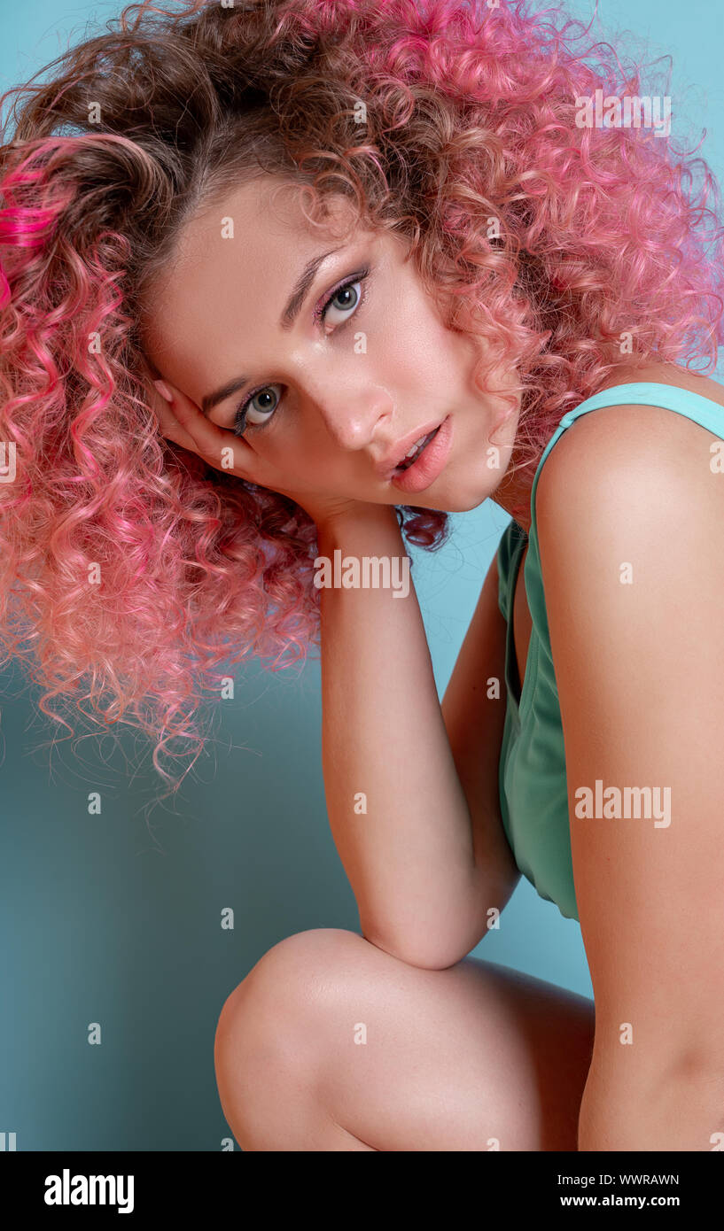 Portrait of beautiful woman with pink curly colored hairs in blue swimsuit. Glitter makeup. 90s style. Ombre. Isolated on blue background Stock Photo