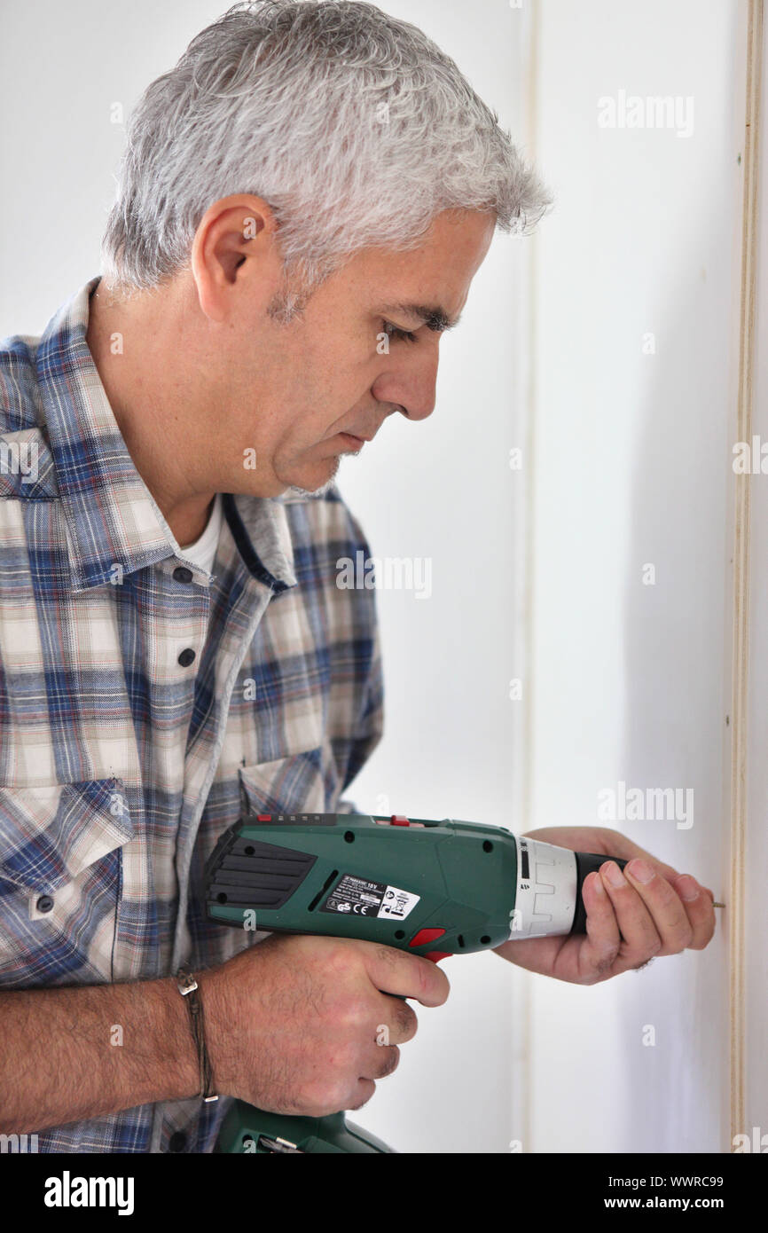 Grey- haired man drilling hole in wall Stock Photo