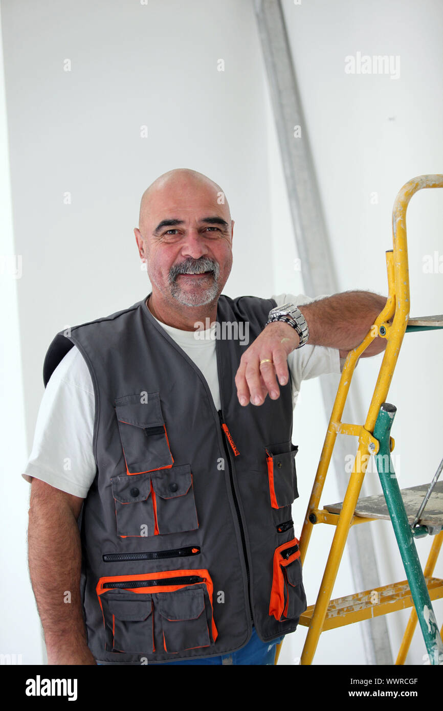 Bald handyman posing by ladder Stock Photo