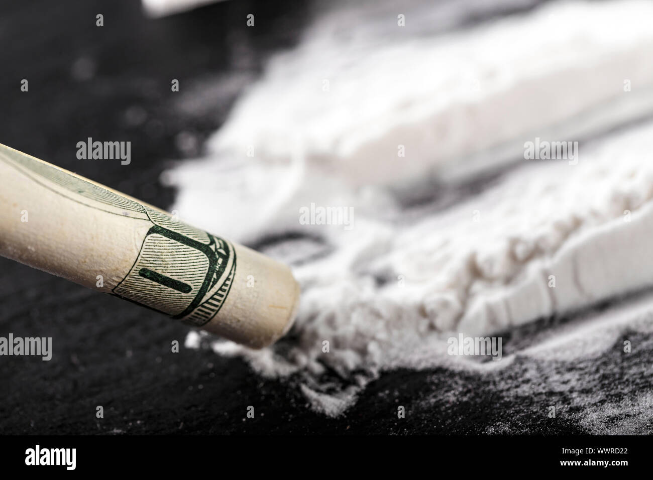 white powder of the drug is scattered on a black table, next to a bill  twisted into a tube. place for text Stock Photo