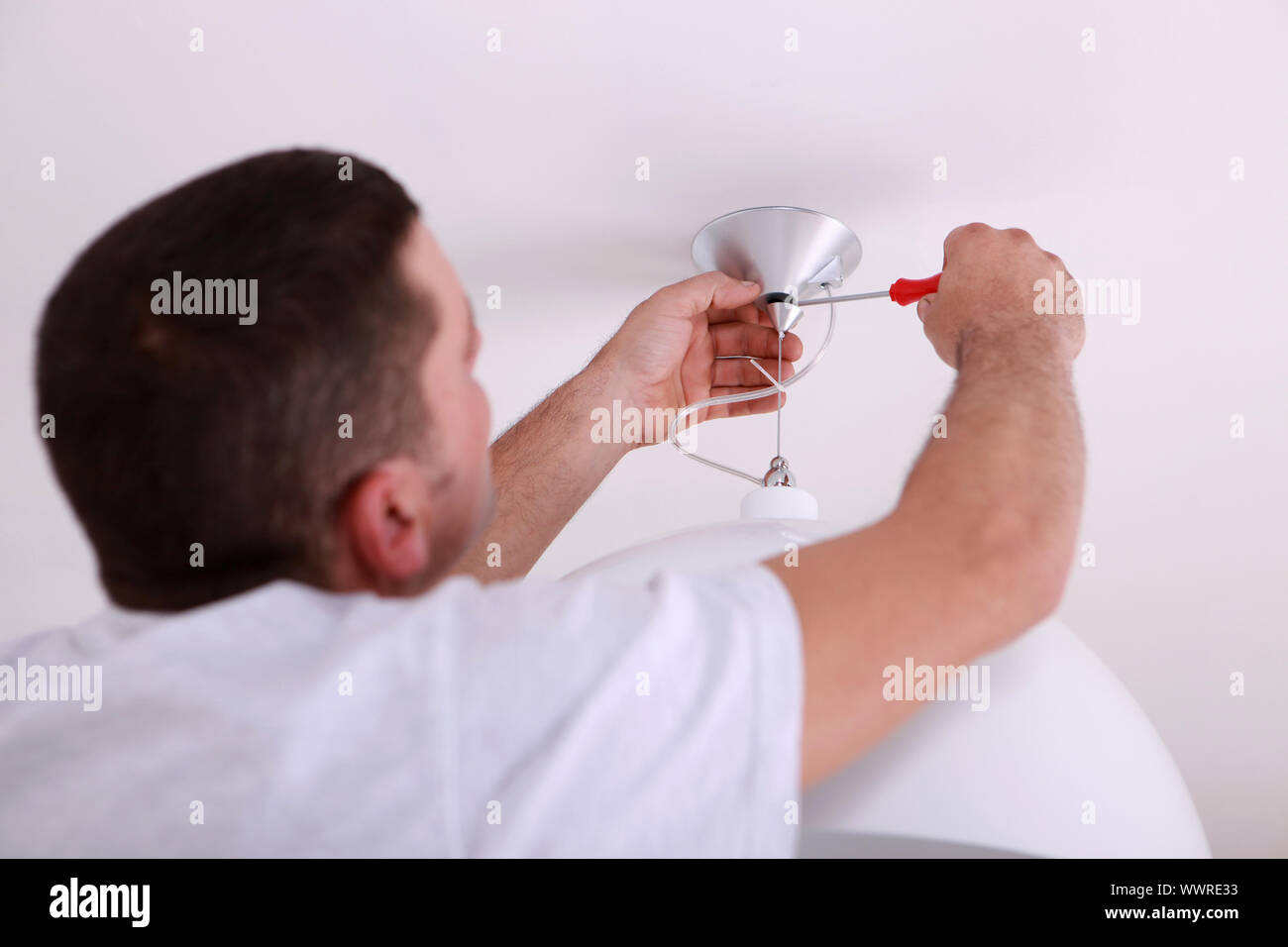 Man repairing ceiling light with screwdriver Stock Photo