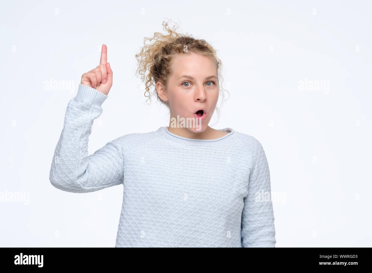 Young beautiful curly girl looking excited holding her mouth opened pointing up having idea. Studio shot. Look here it is amazing concept Stock Photo